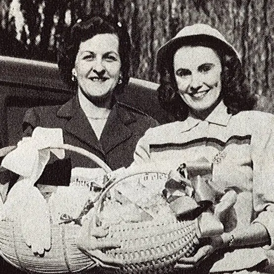 vintage black and white photo of two smiling women holding gift baskets